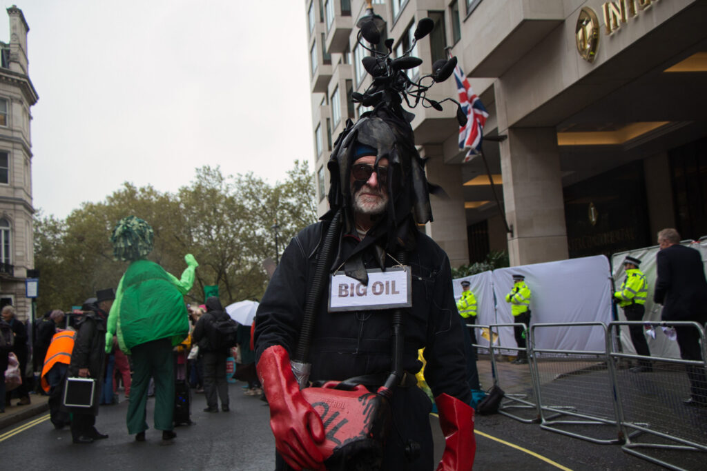 A protestor in balck overalls stands at a distance from the main climate protest