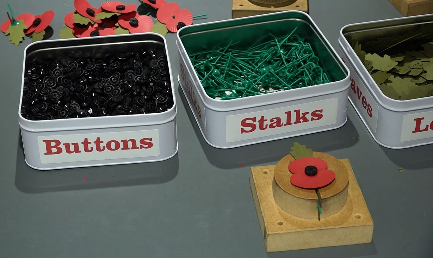 The supplies that are used to make the poppy wreaths, including buttons, stalks, and leaves.