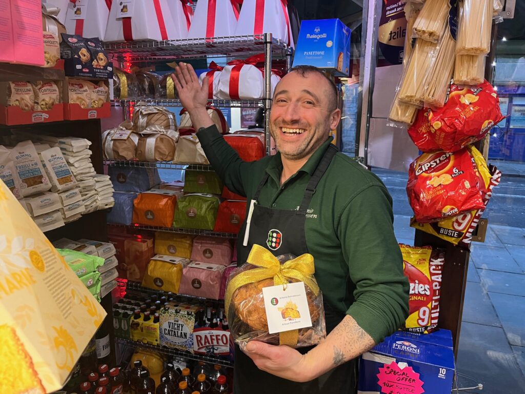 Antonio Nigro smiles holding a panettone and gestures to more