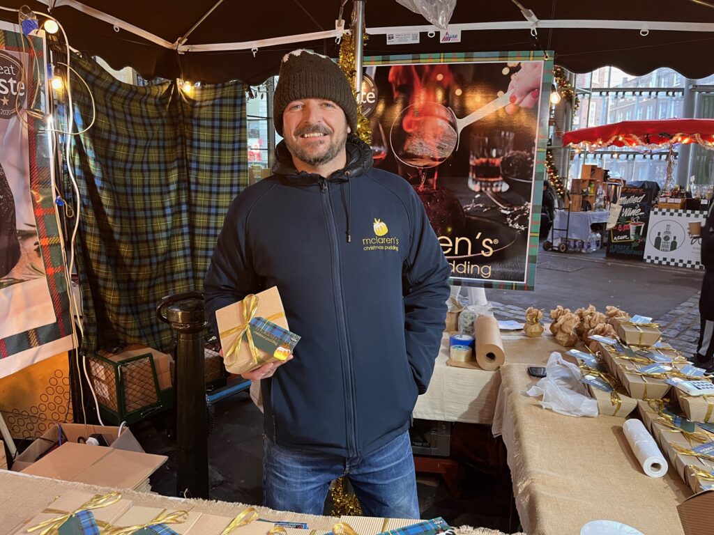 Duncan McLaren stands holding a packaged Christmas pudding in his stall at Borough Market