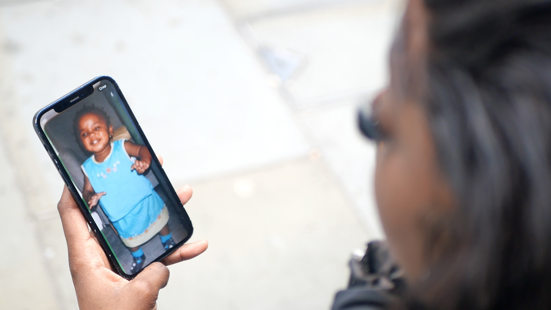 Toyin Odumala, who was abandoned as a baby, looks at a photo of herself as a child on a phone. In the photo the baby is smiling wearing a blue baby outfit. 