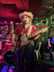 Singer Claudia Kate sings wiht a guitar and a pink cowboy hat