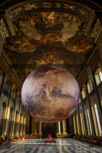 The realistic bronze planet titled 'Mars' hangs in the Painted Hall in the Old Royal Naval College, underneath a detailed painted ceiling.