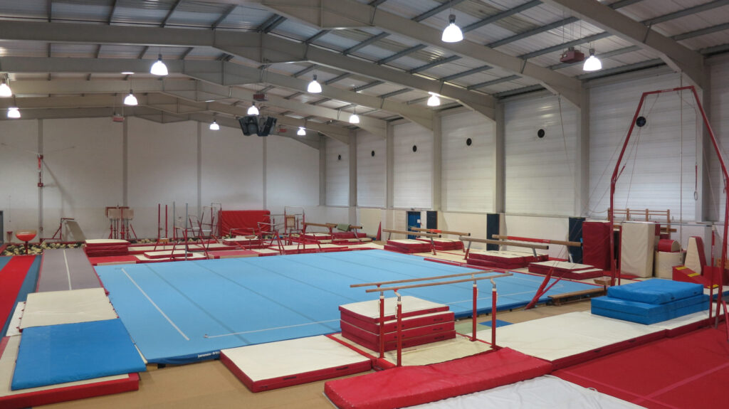 A large hall with high ceilings filled with mats and gymnastics equipment.