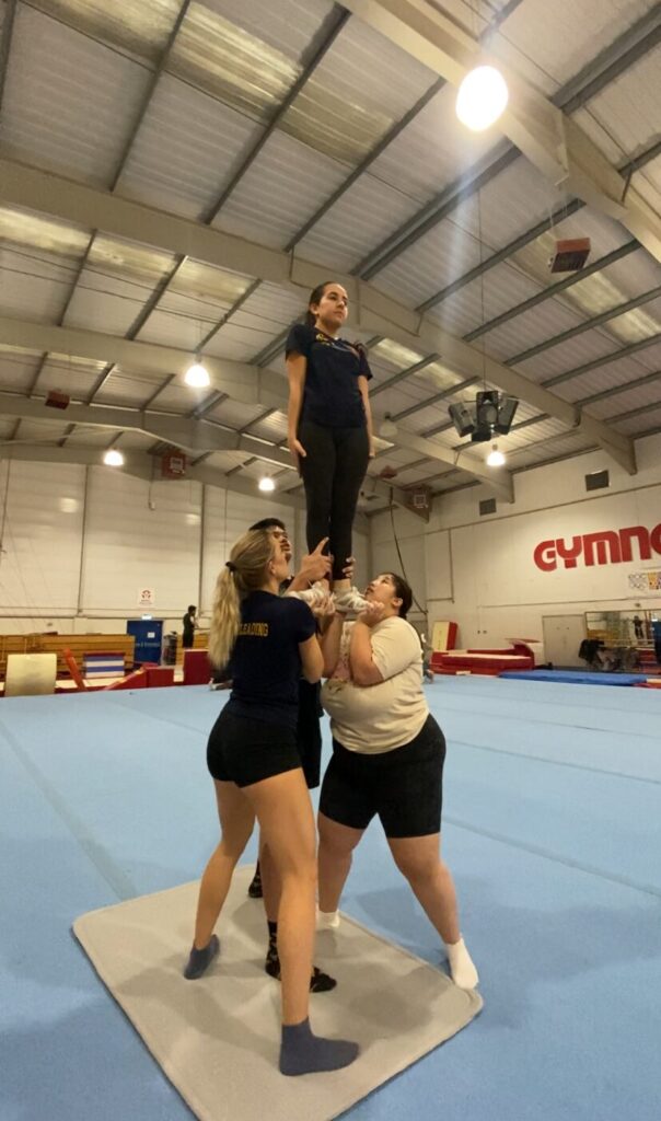 Cheerleaders in a stunt group holding up an individual with extended arms