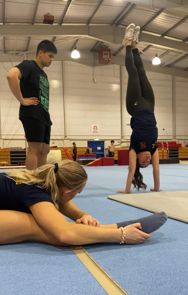 someone is doing a handstand in a gymnastics centre, another person is stretching on the floor.