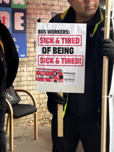 A bus driver at the protest holding a sign saying ‘Bus Workers: Sick &amp; Tired of being Sick &amp; Tired!’