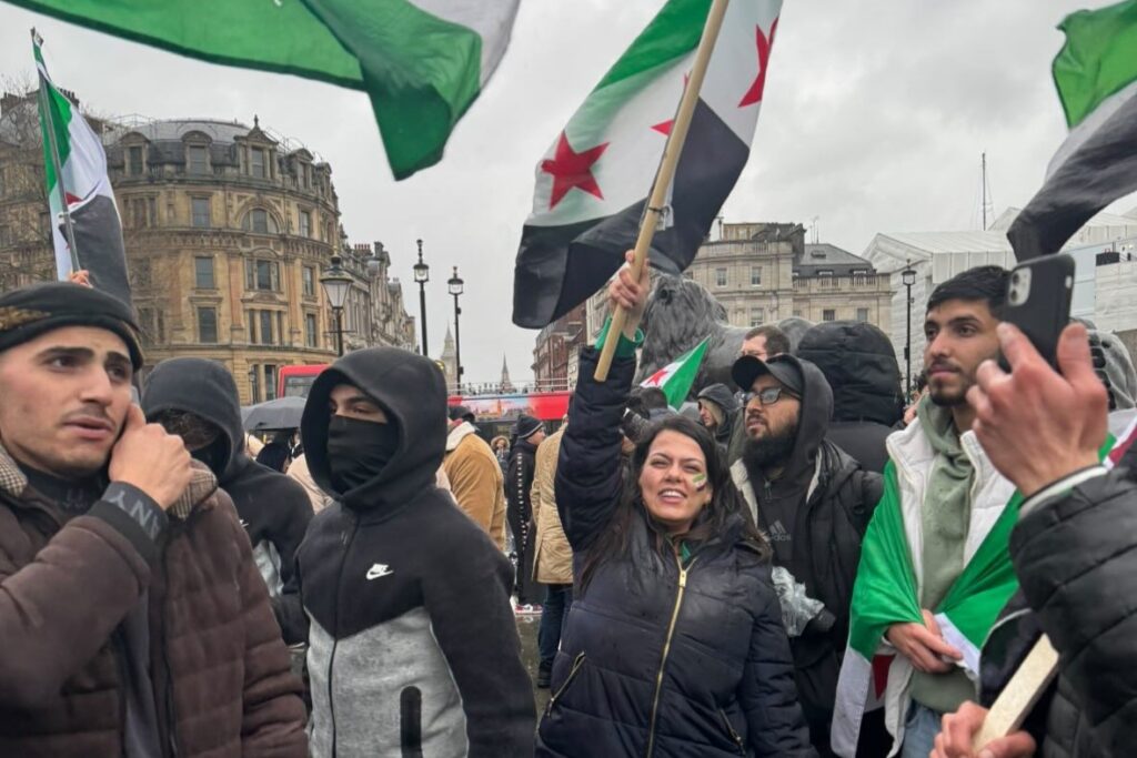 A woman stands in a crowded square holding aloft a Syrian flag.