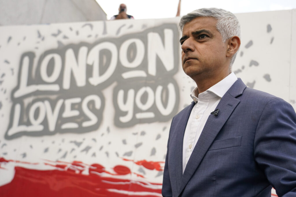 London Mayor Sadiq Khan in front of poster with words "London Loves You"