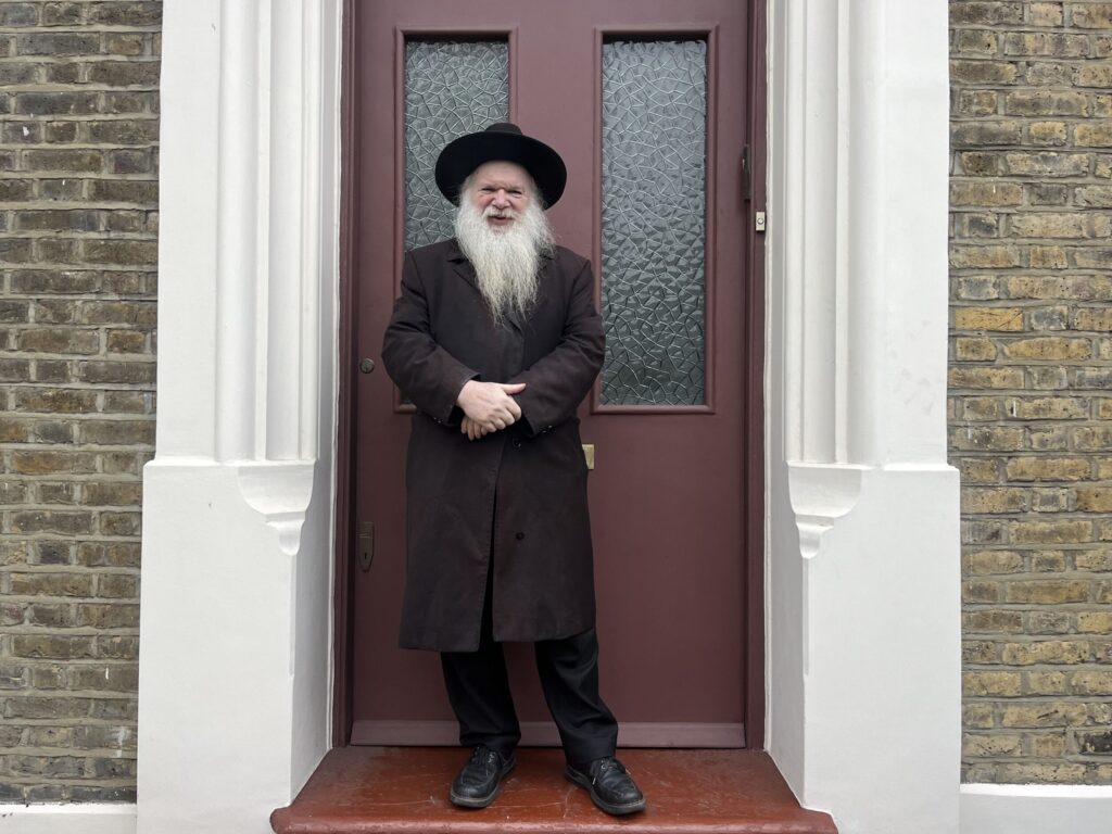 Rabbi Herschel Gluck OBE standing outside of a house.