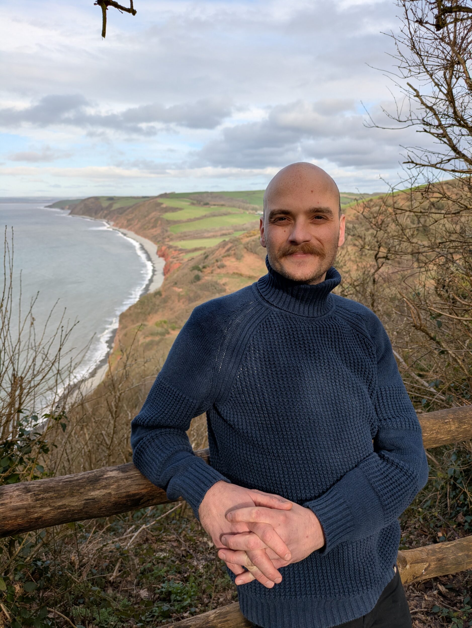 Man smiling at camera by the sea standing on a cliff.